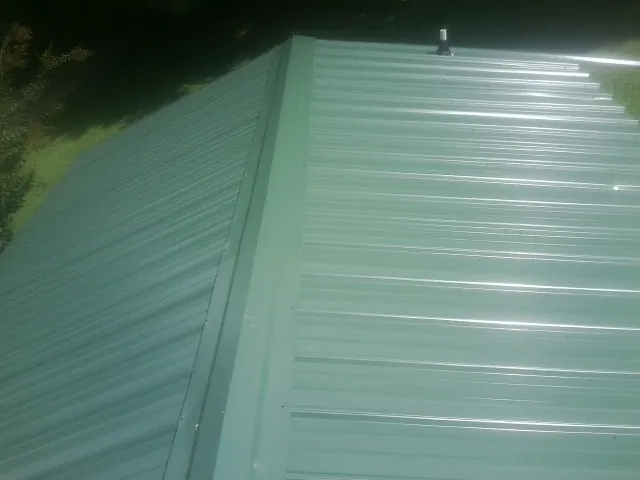 New green metal panels meeting at the ridge of a roof — Flat Roof Repair work by our crew in Gainesville