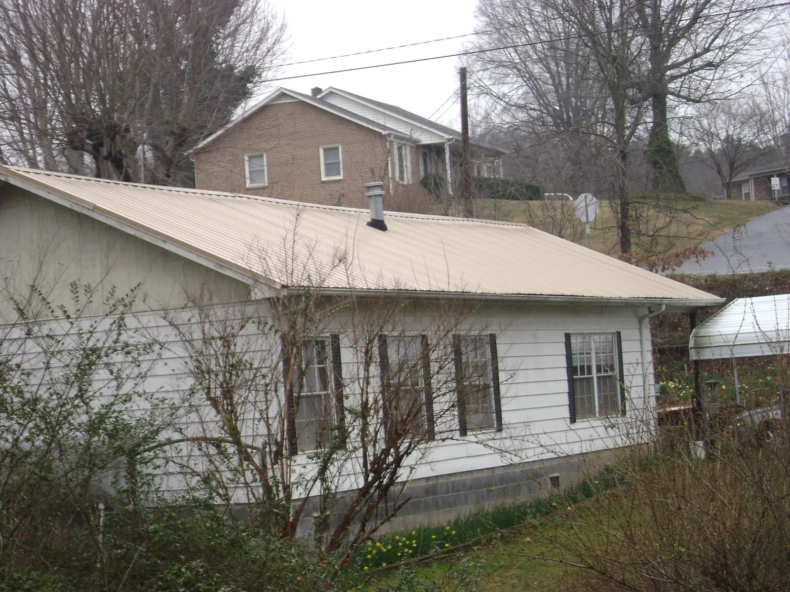 Tan metal roof on a white sided house set into a hillside — Commercial Roofing by Roofing Brothers in Gainesville